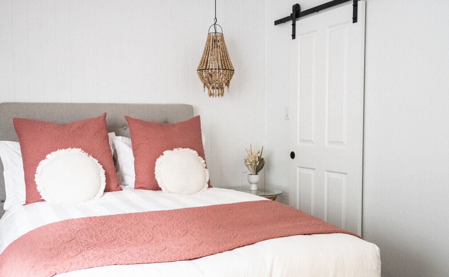 A neatly made bed with a white and pink bedspread, two large pillows, and a hanging light fixture.