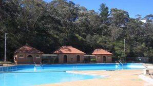 A swimming pool with two small buildings in the background, surrounded by trees. - Original 1895 cottage, magnificent uninterrupted views of valley. (Blackheath)