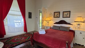 A bedroom with a bed, two bedside lamps, a window with red curtains, and a door leading outside. - Original 1895 cottage, magnificent uninterrupted views of valley. (Blackheath)