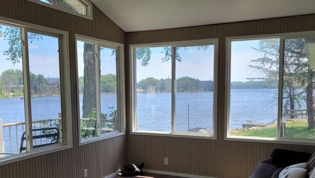 A room with large windows overlooking a lake, a dark wood floor, and a brown sofa with a throw blanket. - Beautiful Riverfront Home near Celebrations. Excellent eagle viewing! (La Crosse)