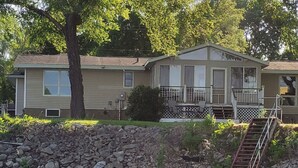 A two-story house with a stone retaining wall and a wooden staircase leading to a deck. - Beautiful Riverfront Home near Celebrations. Excellent eagle viewing! (La Crosse)