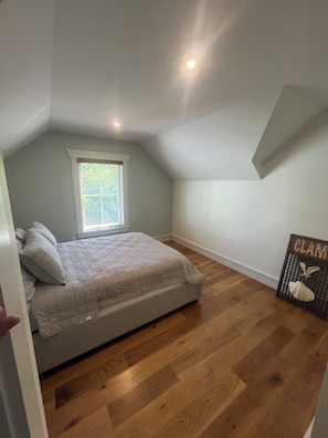Un dormitorio con una cama, una ventana y piso de madera.