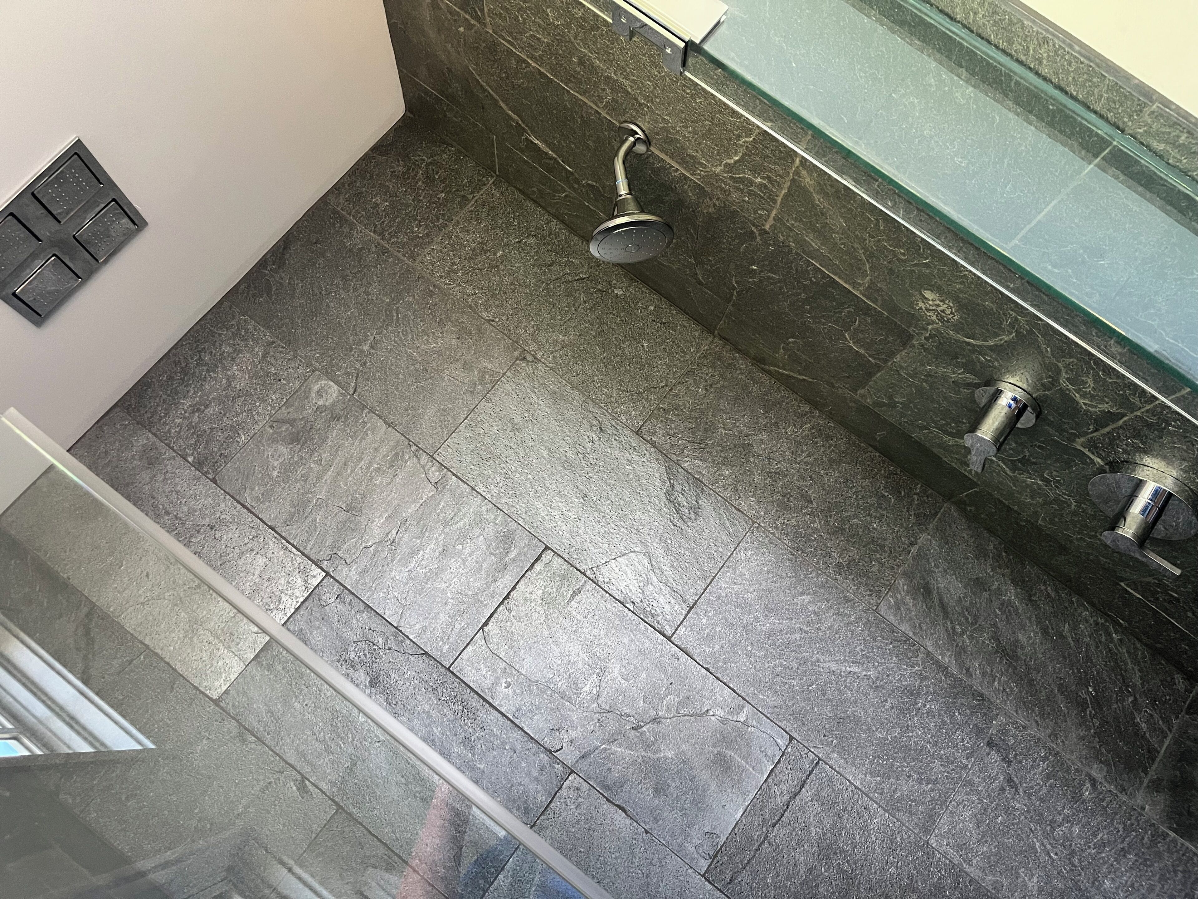 A bathroom with a shower, a glass-enclosed sink, and a tiled floor.