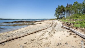 A sandy beach with a rocky shoreline and a forested area.