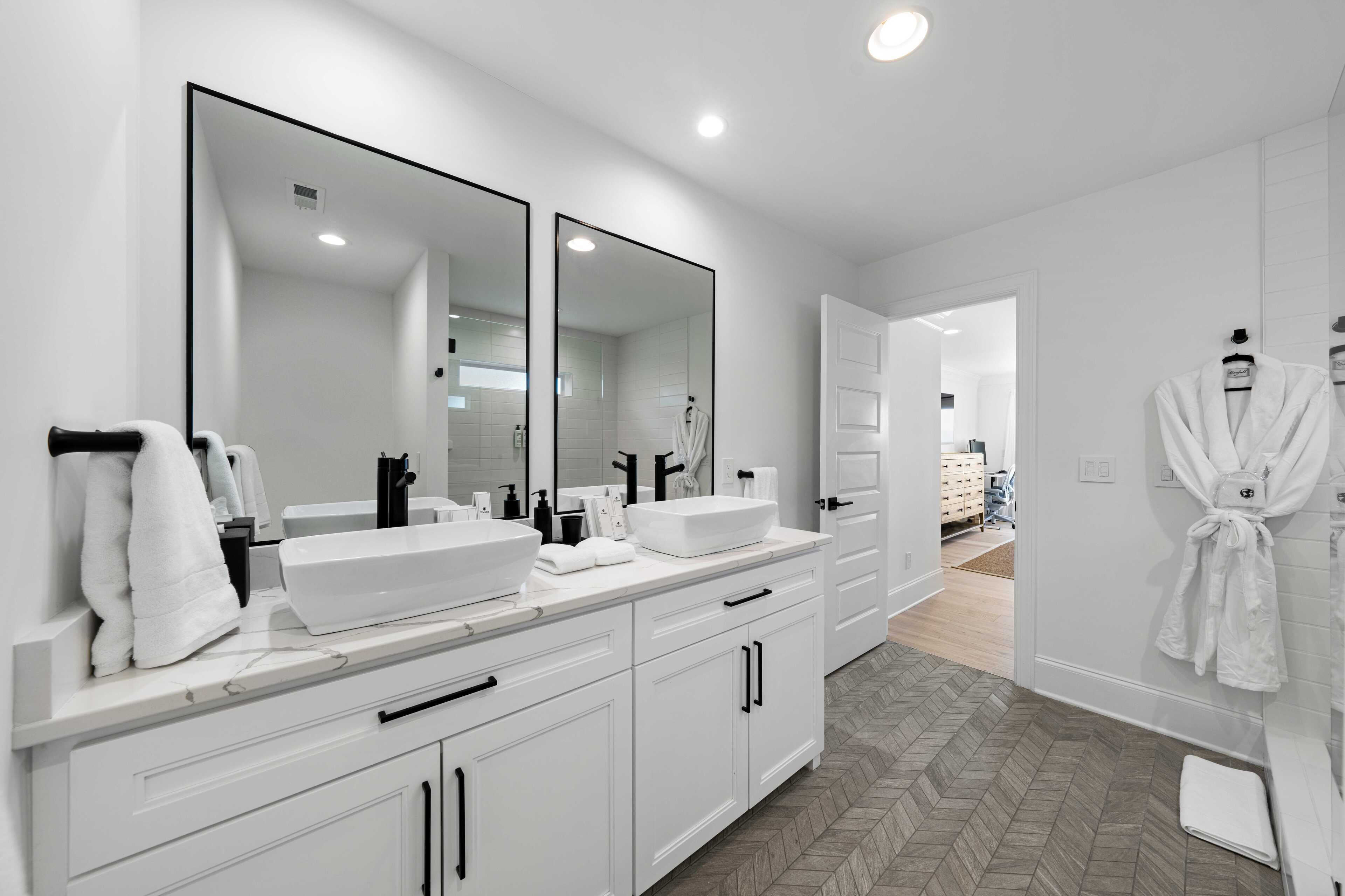 A modern bathroom with two large mirrors, a white vanity, and a walk-in shower.