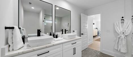 A modern bathroom with two large mirrors, a white vanity, and a walk-in shower.