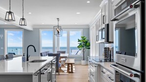 A modern kitchen with a large island, stainless steel appliances, and a view of the ocean. - Kure Beach Ocean View, Pool & Beach Access (Kure Beach)