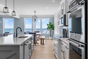 A modern kitchen with a large island, stainless steel appliances, and a view of the ocean.