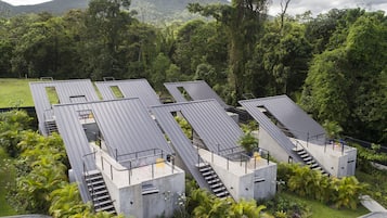 Um edifício moderno com vários níveis, estruturas de concreto e escadarias, cercado por vegetação exuberante e uma montanha ao fundo.