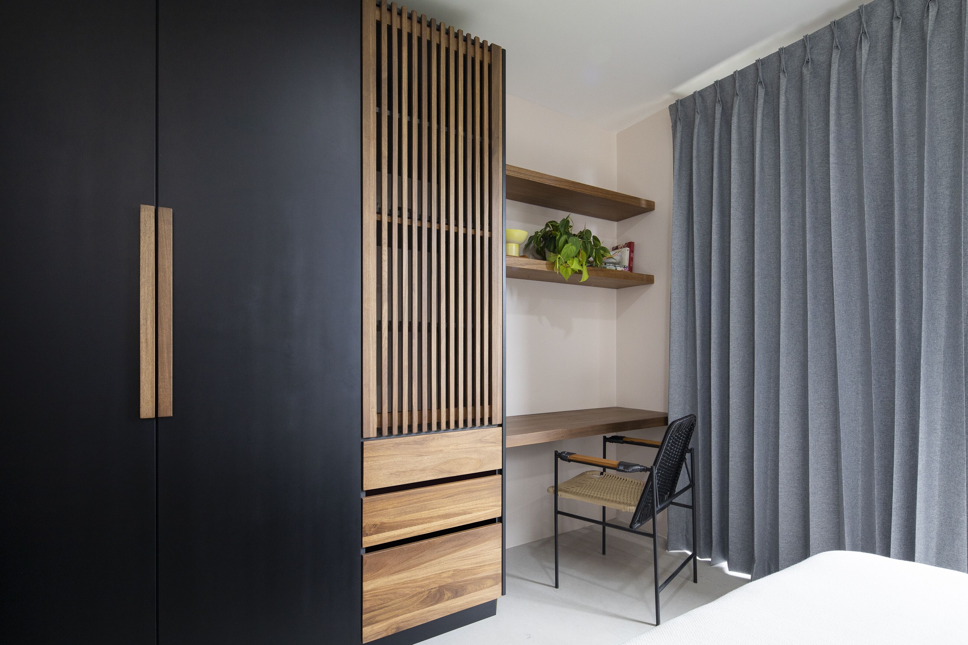 A modern bedroom with a dark wardrobe, a wooden desk, a chair, and a grey curtain.