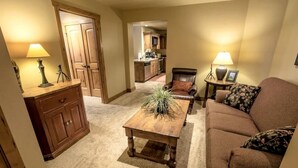 A cozy living room with a brown leather sofa, a wooden coffee table with a plant, a wooden cabinet, and a kitchen in the background. - Mountain Rustic Perfection in Prime Locale (Park City)