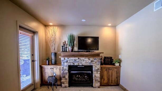 A living room with a stone fireplace, a television mounted above it, and a door with blinds. - Mountain Rustic Perfection in Prime Locale (Park City)