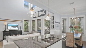 Una cucina moderna con una grande isola, mobili bianchi e una zona pranzo con sedie in vimini.