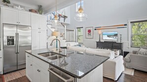 Una cucina moderna con isola centrale, elettrodomestici in acciaio inossidabile e zona pranzo con divano e televisore.
