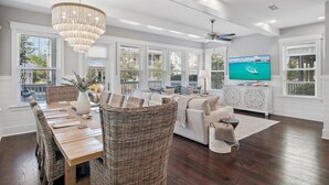 A spacious living room with a large TV, wicker furniture, and a chandelier. - Rosé Sunsets 6 Seaters Golf Cart and 5 Bikes, Heated Resort Pools, Pickleball Courts (Santa Rosa Beach)