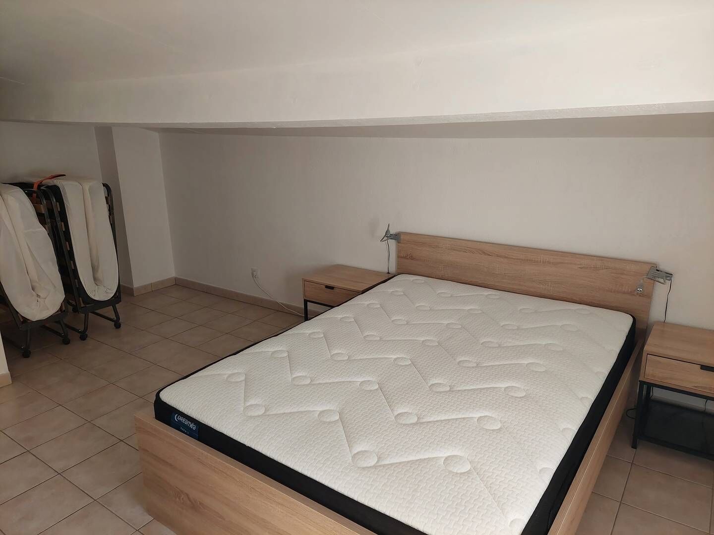 Een slaapkamer met een houten bed, een nachtkastje en een wandplank.