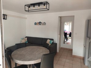 Un comedor con una mesa redonda y sillas, un sofá oscuro con cojines, y una lámpara fijada en la pared.