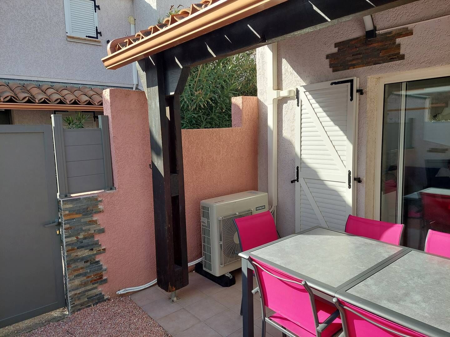 Un patio con mesa y sillas, un equipo de aire acondicionado integrado y una puerta de cristal que da a un espacio interior.