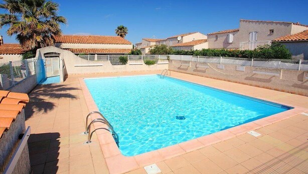 A rectangular swimming pool with clear blue water, surrounded by a tiled deck and a white fence. - Pretty villa T4 aircon swimming pool Rochelongue Cap d'Agde (LE CAP D AGDE)