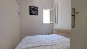 A small, narrow room with a single bed, a window, and a wall-mounted picture. - Pretty villa T4 aircon swimming pool Rochelongue Cap d'Agde (LE CAP D AGDE)
