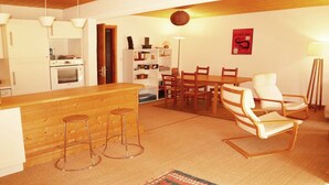 Una cuina moderna amb armaris blancs, una illa de fusta amb tamborets i una zona de menjador amb cadires i taula de fusta.