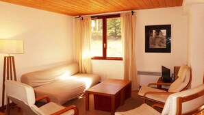 Habitació acollidora amb un sofà, dues butaques, una taula de fusta, una làmpada i una televisió.