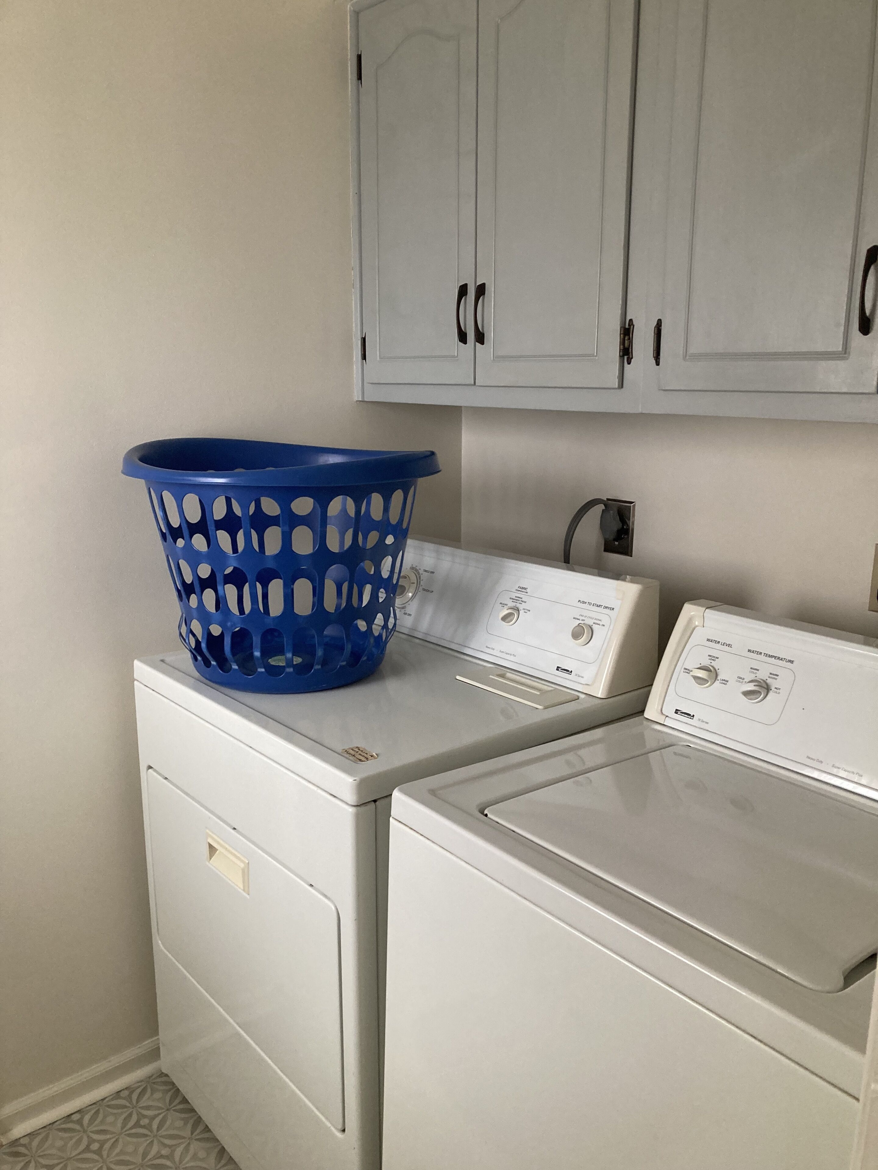 A laundry area with a blue laundry basket on a washing machine and a dryer.