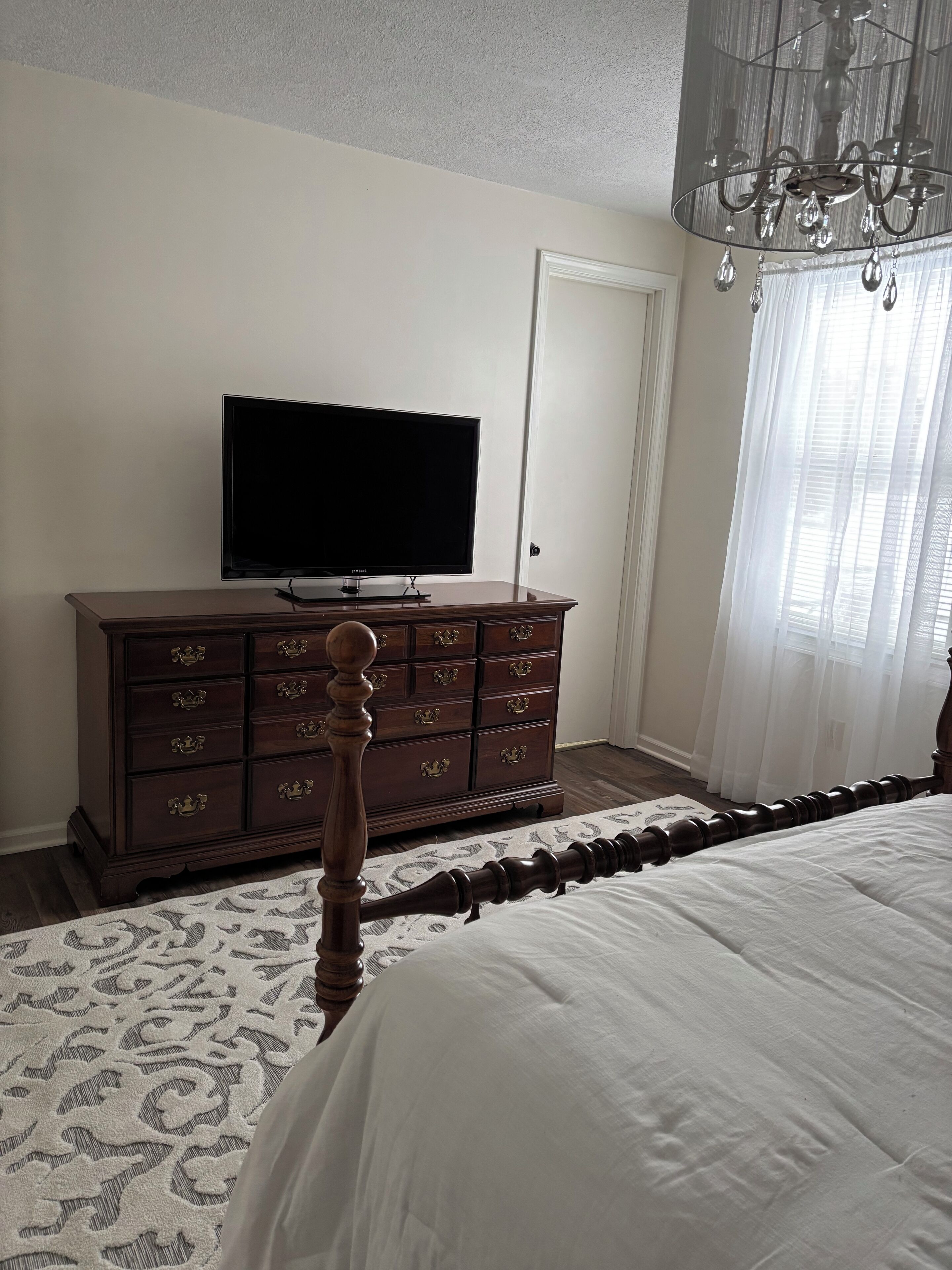 Ein Schlafzimmer mit einem Bett, einem Schminktisch, einem Fernseher und einer Kandelaber.