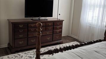 Ein Schlafzimmer mit einem Bett, einem Schminktisch, einem Fernseher und einer Kandelaber.