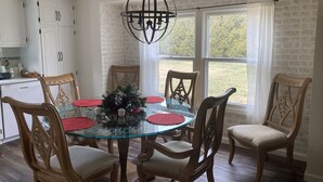 Un coin repas avec une table en verre entourée de chaises en bois, un lustre et un mur en briques.