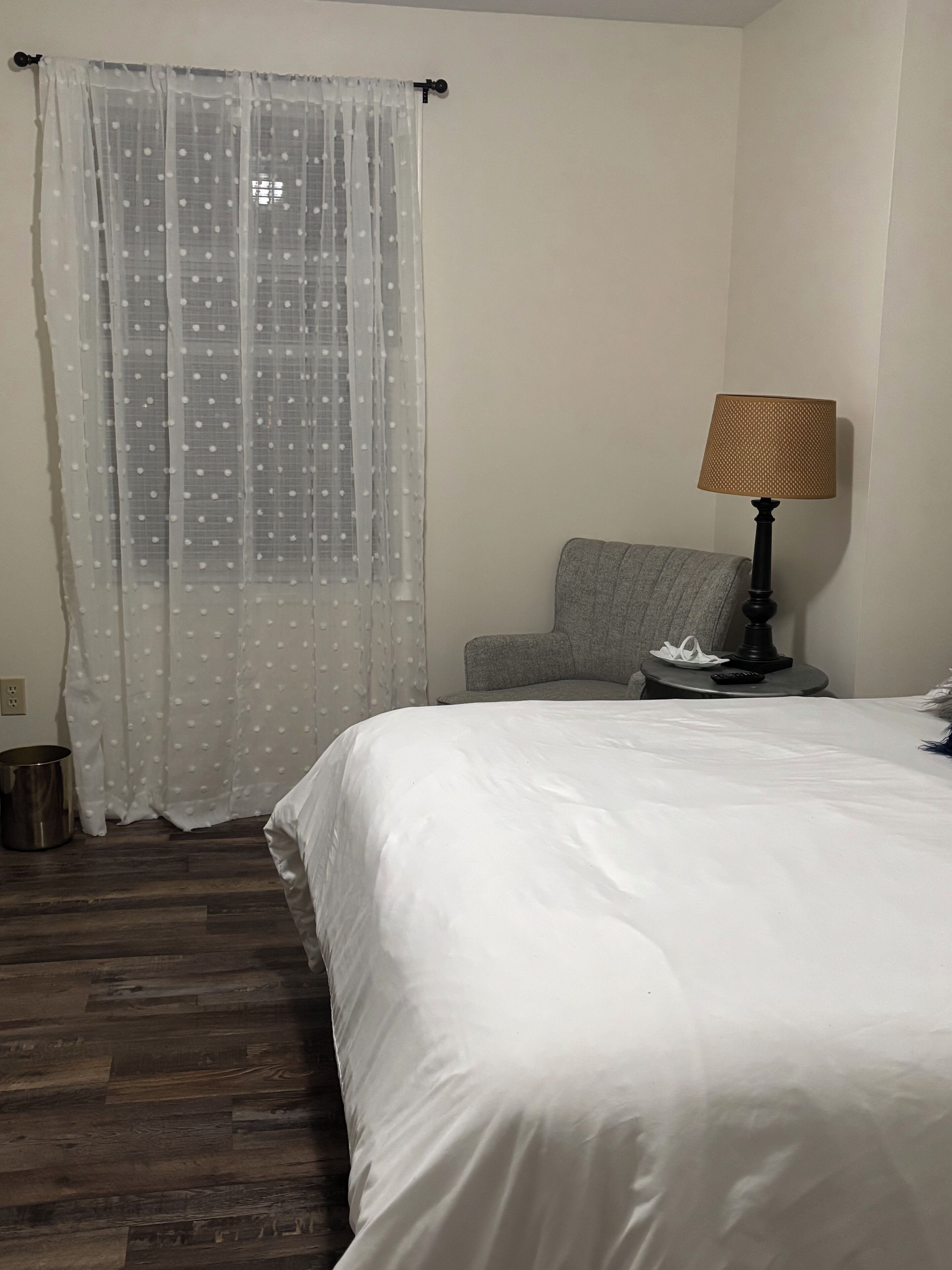A bedroom with a bed, a chair, a lamp, and a curtain.
