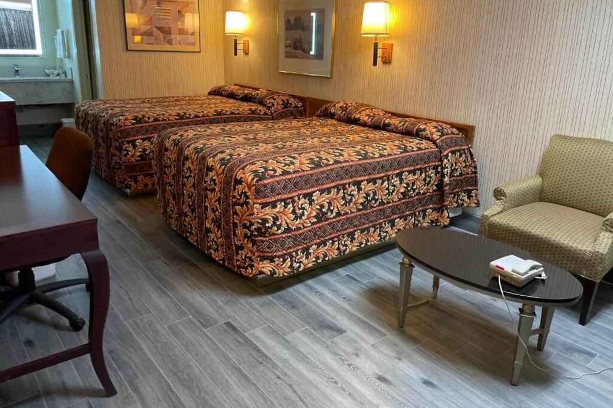 Quarto de hotel com duas camas, uma mesa de jantar, uma mesa redonda pequena e uma cadeira.