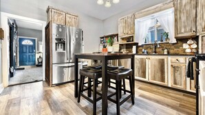 A kitchen with wooden cabinets, a stainless steel refrigerator, a bar stool, and a chandelier.
