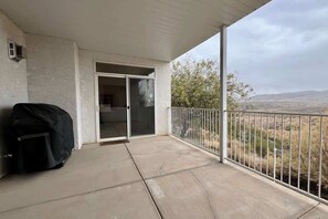Ein überdachter Balkon mit einer Schiebeglastür, einem Grill und Blick auf eine hügelige Landschaft.