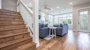 A spacious living area with a wooden staircase, a gray sofa set, and a small round table.