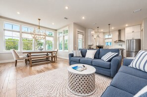 A spacious living room with a blue sofa, a dining table, and a kitchen in the background.