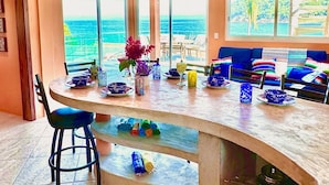 A modern kitchen with a curved island, large windows, and a view of the ocean.