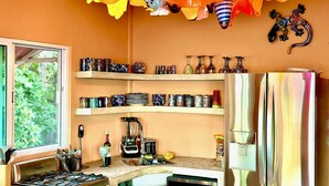 A kitchen with a gas stove, microwave, and a refrigerator. There are shelves with various kitchenware and a window with a view of greenery.