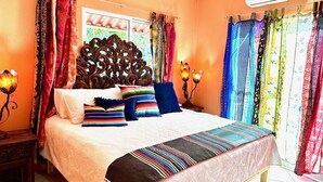 A bedroom with a large bed, ornate headboard, colorful curtains, and a decorative lamp.