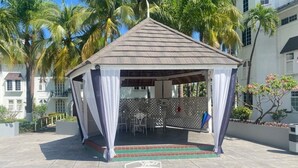 Un belvédère doté d’un patio carrelé, de rideaux blancs et d’une table en verre.