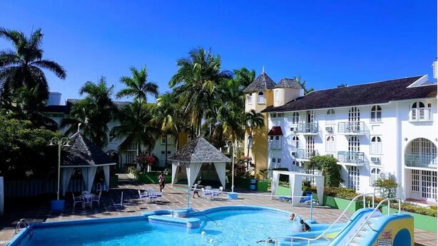 Un espace piscine d’hôtel avec une piscine à l’eau cristalline, des chaises longues et des palmiers.