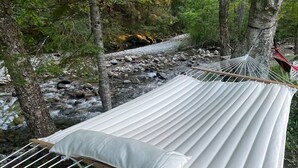 A hammock set up between trees by a stream. - Maple Castle – Cozy Riverside Retreat with Hot Tub, Trails & Fireplace (Hancock)