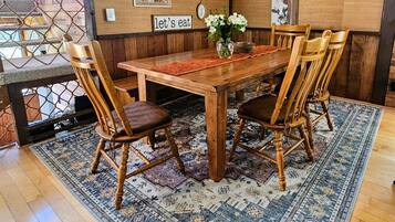 A dining area with a wooden table, four chairs, a rug, and wall decorations including a clock and a framed picture.