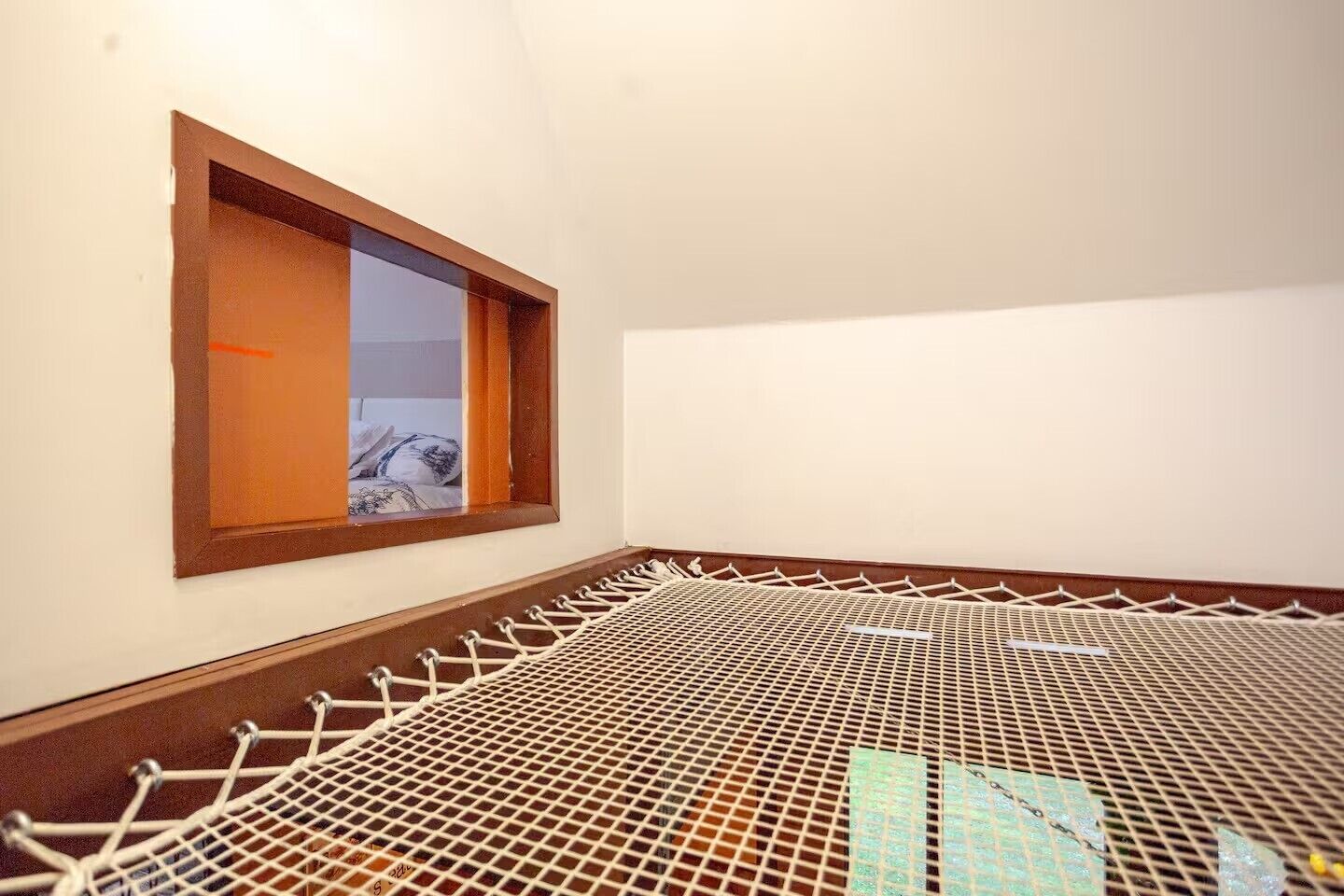 Une pièce avec une fenêtre, un lit et un plancher en métal grillagé.