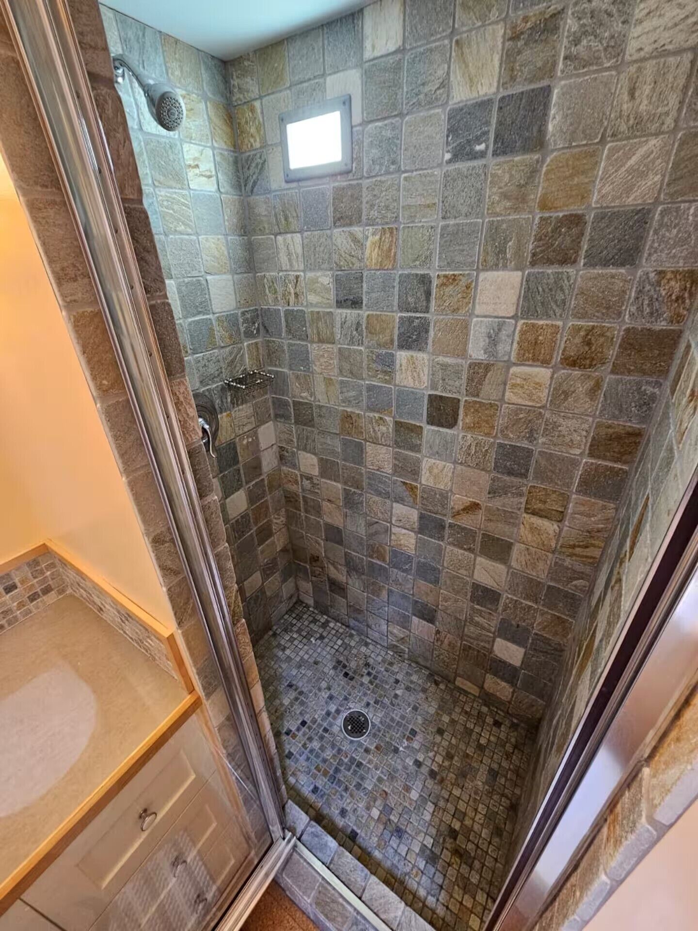 Ducha con azulejos de piedra y puerta de cristal.