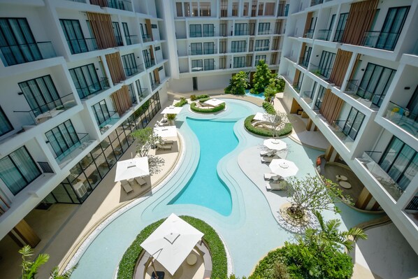 Un hotel moderno con piscina central, varios balcones y zonas de estar al aire libre.