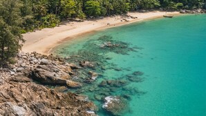 An aerial view of a beach with clear turquoise waters, rocky shoreline, and dense tropical vegetation. - Radisson Resort Layan Phuket (Choeng Thale)