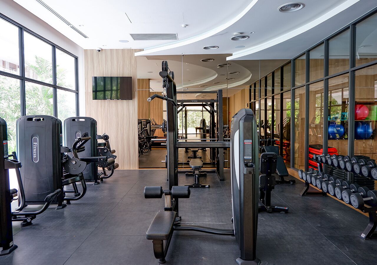 A modern gym with various exercise equipment, large windows, and a view of outdoor greenery.