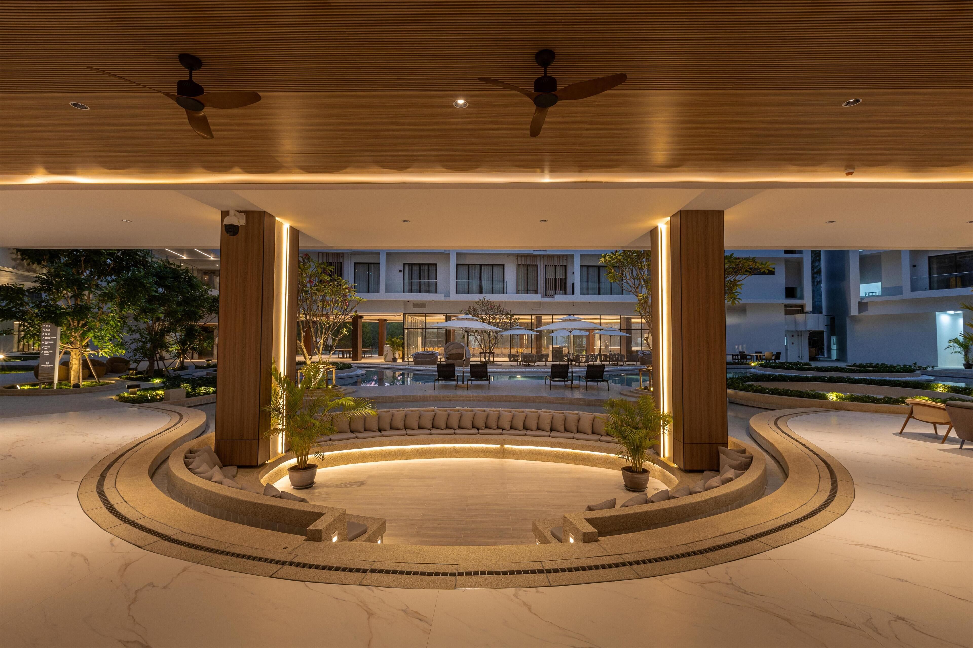 En modern hotelllobby med en pool, sittgrupper och utsikt över byggnadens fasad.