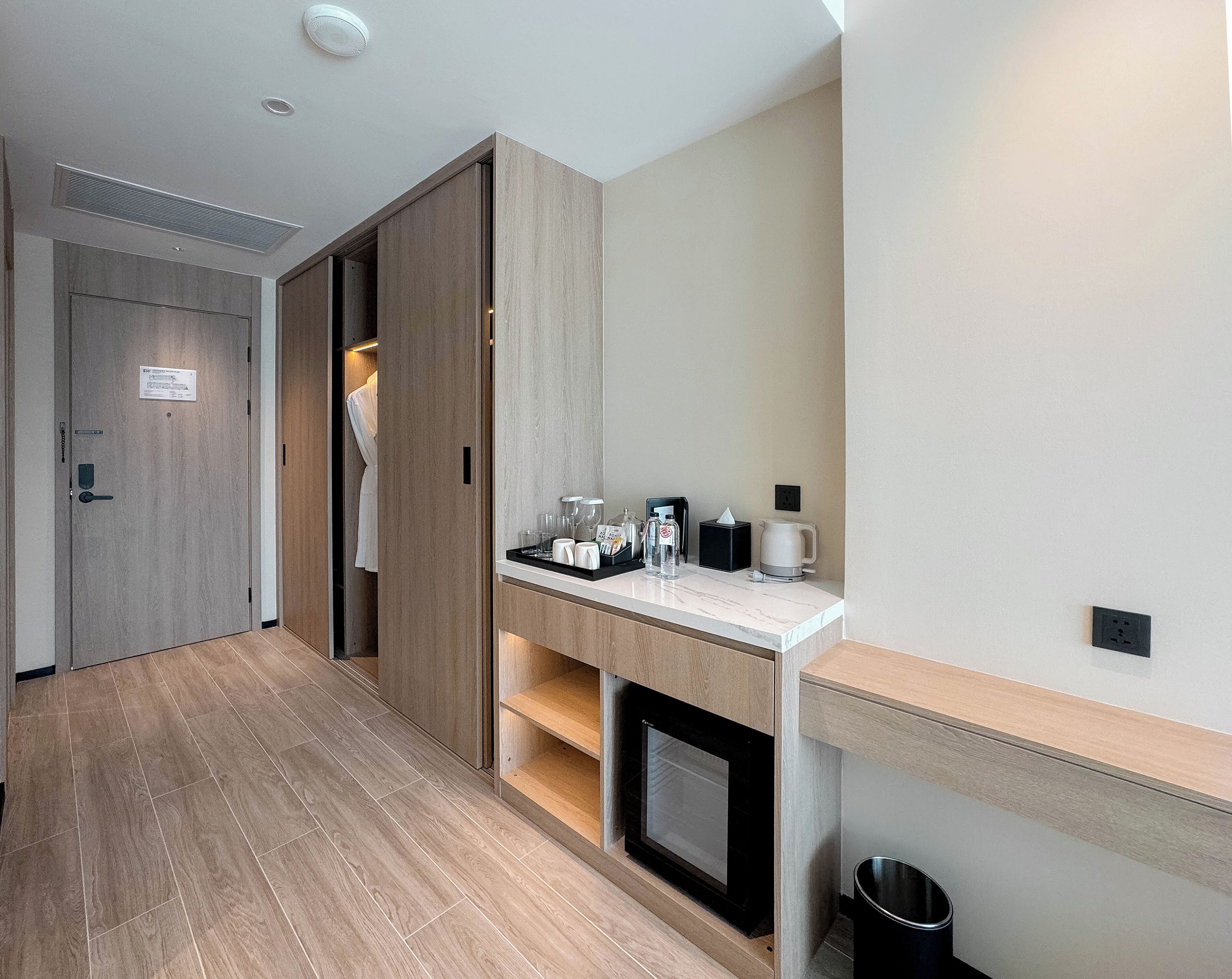 A hotel room with a wooden floor, a minibar, a microwave, and a small trash bin.